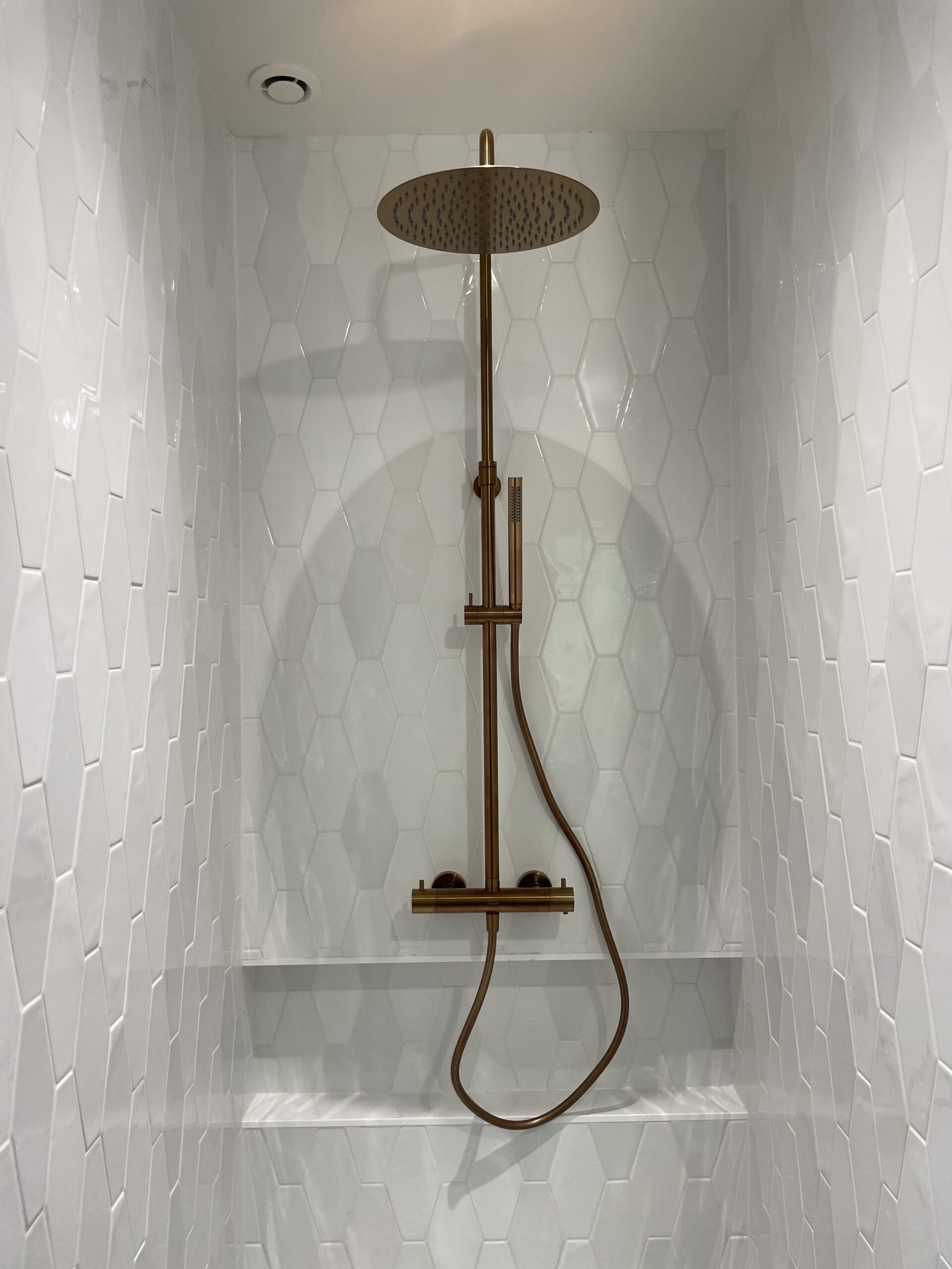 Pose d'une magnifique colonne de douche apparente couleur bronze brossé dans une douche avec un carrelage mosaïque.